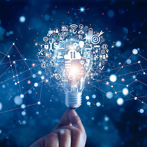 Eine Hand, die eine Glühbirne mit einem digitalen Netzwerk und verschiedenen Symbolen zum Thema Innovation und Technologie hält, die vor einem dunkelblauen Hintergrund davon ausgehen.