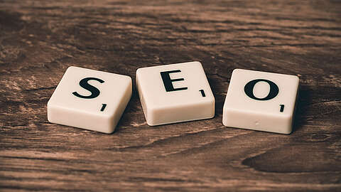 SEO Drei Scrabble-Steine mit dem Wort „SEO“ auf einer Holzoberfläche.