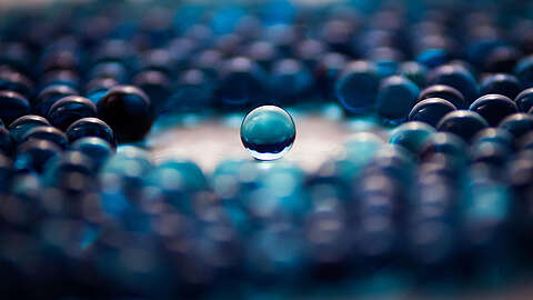 Individuelle Softwareentwicklung für Unternehmen Eine einzelne klare blaue Murmel hebt sich scharf ab und ist von vielen unscharfen blauen Murmeln im Hintergrund umgeben, was einen starken visuellen Kontrast erzeugt.