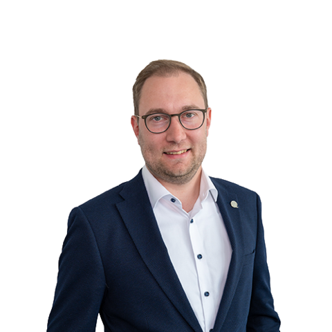 Ein Mann mit kurzen braunen Haaren und Brille, der ein weißes Button-Down-Hemd trägt, lächelt in die Kamera vor einem schlichten weißen Hintergrund.