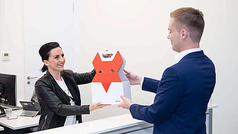 Besuchermanagement - Die Herausforderung Empfangsdame begrüßt Gast und gibt ihm eine Q-FOX® Tüte