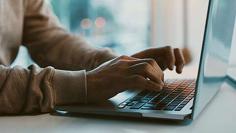 Person im Pullover sitzt am Laptop und tippt in die Tastatur