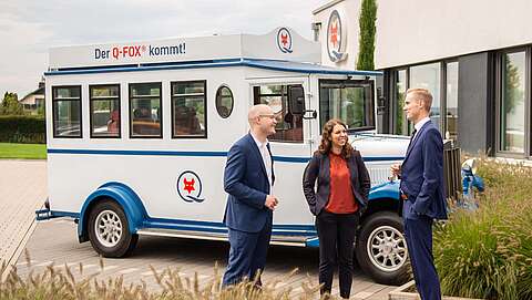 3 Leute stehen vor einem Q-FOX® Bus