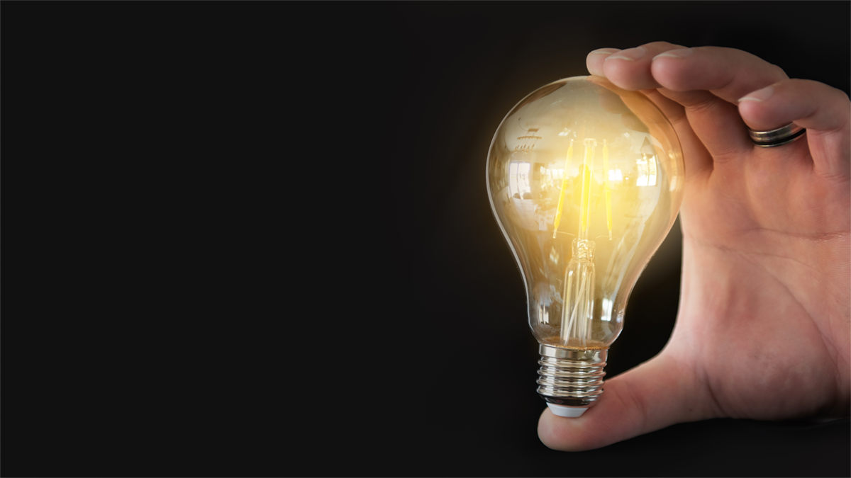 Prototypenentwicklung mit Lean Startup - Methoden | HEDGEHOG Eine brennende Glühbirne wird in einer Hand gehalten auf schwarzem Hintergrund